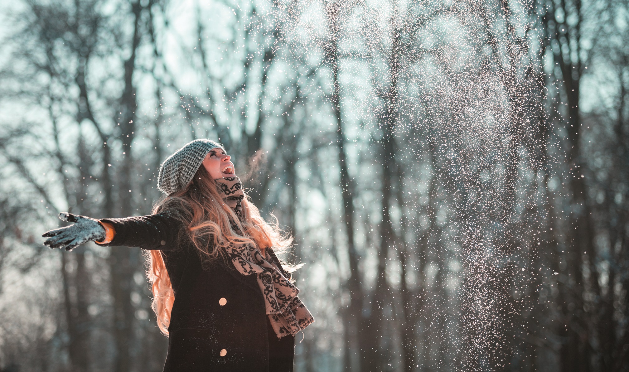 Smiling woman throwing snow in the air at sunny winter day